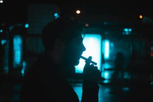 Silhouette of a man smoking a cigarette in an urban environment at night, captured in moody lighting.